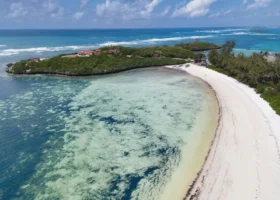 Splendida veduta panoramica della baia di Watamu antistante il Barracuda Inn Resort, con l'acqua cristallina dalle tonalità turchesi e azzurre che si infrange sulla spiaggia di sabbia bianca deserta sotto un cielo azzurro e limpido.