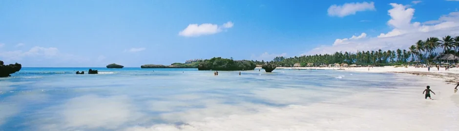 Veduta panoramica sull'oceano Indiano turchese e trasparente dalla costa del Barracuda Inn Resort, con la caratteristica battigia di sabbia chiara e fine lambita da piccole onde calme sotto un cielo sereno.