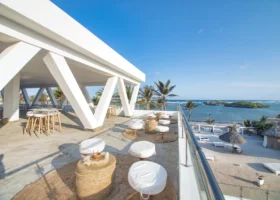 Terrazza coperta rialzata del Barracuda Inn Resort con pavimento in legno e una ringhiera protettiva, che offre una spettacolare vista panoramica sul giardino tropicale di palme, sulla spiaggia bianca sottostante e sulle acque azzurre di Watamu.