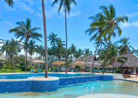 Grande piscina all'aperto con mosaici azzurri circondata da alte palme da cocco e aree relax a pochi passi dalla spiaggia del resort