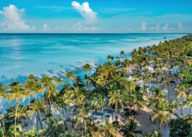Veduta aerea panoramica del resort Diamonds Mapenzi Beach a Zanzibar, che mostra i bungalow bianchi immersi in un fitto palmeto tropicale lungo una spiaggia di sabbia chiara e le ampie sfumature turchesi dell'oceano Indiano sotto un cielo azzurro.