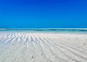 Spettacolare e luminoso panorama marino di Watamu di fronte al Jacaranda Beach Resort, con le caratteristiche increspature della sabbia bianca lasciate dal fenomeno della bassa marea, bagnate da una distesa di acqua cristallina e trasparente che si estende sotto un cielo azzurro e limpido.