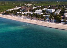 Spettacolare fotografia aerea scattata con drone che mostra l'intera estensione del Jacaranda Beach Resort a Watamu, situato lungo una linea costiera di sabbia chiara e bagnato da un mare turchese sfumato, con i blocchi di edifici bianchi immersi nella vegetazione tropicale e circondati dalla natura del Kenya.