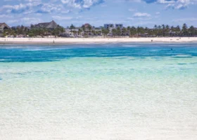 Splendida veduta del mare turchese e cristallino di Watamu di fronte al Jumbo Resort, con l'acqua trasparente che sfuma nel blu profondo, una lunghissima lingua di sabbia corallina chiara all'orizzonte costeggiata da palme e strutture tipiche.