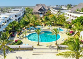 Spettacolare veduta aerea panoramica della struttura del Jumbo Resort a Watamu, che mette in evidenza la piscina circolare centrale circondata da giardini fioriti, palme e i blocchi di edifici bianchi in stile moresco con tetti in makuti.