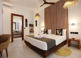 Interno di una moderna ed elegante camera da letto del Karafuu Beach Resort con letto matrimoniale, cigni di asciugamano, dettagli in legno e soffitto con ventola