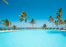 Ampia piscina azzurra del resort circondata da lettini prendisole e palme da cocco sotto un cielo azzurro e limpido