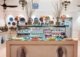 Un ricco buffet con alzate di pasticceria, fette di anguria, melone e piatti decorativi blu arabi appesi alla parete del Marijani Beach Resort