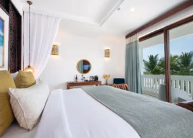 Interno di una luminosa camera da letto del Marijani Beach Resort con tessuti azzurri e una grande porta finestra scorrevole affacciata sulle palme