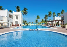 Una grandissima piscina azzurra circondata da lettini e palme da cocco sotto un cielo azzurro limpido al Marijani Beach Resort