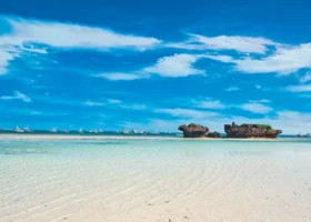 Spettacolare veduta della spiaggia del Medina Palms durante il fenomeno della bassa marea, con una distesa di sabbia bianca finissima bagnata da un velo d'acqua cristallina. In mezzo al mare emergono formazioni rocciose coralline e numerose barche ancorate all'orizzonte sotto un cielo azzurro.