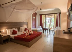 Interno di una camera da letto mini suite del My Blue Hotel con letto matrimoniale decorato da cigni di asciugamani e petali rossi sotto una zanzariera