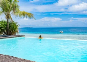 Ospite del resort rilassata sul bordo della piscina a sfioro del My Blue Hotel mentre osserva una barca a motore che naviga nell'oceano aperto
