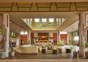 La grande e luminosa hall d'ingresso dell'Hotel Riu Jambo con pavimenti scuri, divani moderni beige, pouf verdi e un grande ventilatore a soffitto