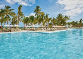 La grandissima piscina d'acqua azzurra dell'Hotel Riu Jambo circondata da lettini prendisole, ombrelloni bianchi e alte palme da cocco