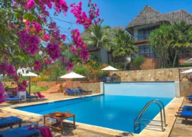 Piscina all'aperto del Sultan Sands Island Resort circondata da lettini prendisole, ombrelloni e piante di bouganville con fiori fucsia accesi