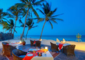 Tavoli apparecchiati con tovaglie rosse su una terrazza in legno del ristorante del Sultan Sands Island Resort all'ora del crepuscolo