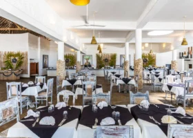 Ampia sala interna del ristorante principale del Watamu Beach Resort, arredata in stile swahili con pilastri rivestiti in pietra, tavoli apparecchiati con tovaglie bianche e nere, sedie in legno decapato e buffet sullo sfondo.