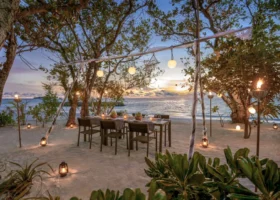 Allestimento per una cena romantica sulla spiaggia al tramonto, con tavolo apparecchiato sotto gli alberi illuminati da lanterne, lampade a sfera e fiaccole accese, affacciato sul mare mentre il sole cala all'orizzonte. Alila Kothaifaru Maldives, Kothaifaru, Atollo di Raa, Maldive.