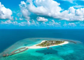 Veduta aerea da drone dell'intera isola di Brennia Kottefaru nell'Atollo di Raa, alle Maldive: laguna turchese, barriera corallina affiorante e spiaggia di sabbia bianca a 360 gradi circondate dal blu intenso dell'Oceano Indiano.