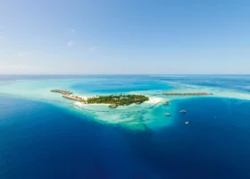 Veduta aerea da drone dell'isola tropicale di Moofushi circondata da una laguna dalle molteplici sfumature di turchese e blu, con file di ville overwater sull'acqua, barriera corallina affiorante, dhoni all'ancora e oceano profondo tutt'intorno; Constance Moofushi, Atollo di Ari Sud, Maldive, Oceano Indiano.