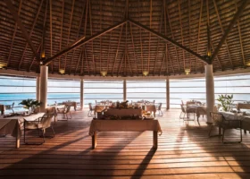Interno del ristorante principale dell'isola di Dhiggiri, nell'atollo di Vaavu alle Maldive, con imponente copertura circolare in makuti su struttura in legno, tavoli apparecchiati in bianco e buffet centrale con frutta tropicale; pavimento in legno, colonne bianche e ampie aperture affacciate sull'Oceano Indiano nella luce calda del tramonto.