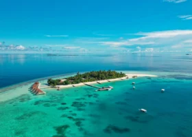 Veduta panoramica aerea dell'intera isola di Maayafushi con vegetazione tropicale, spiaggia di sabbia bianca, over water bungalow e dhoni maldiviani ormeggiati nella laguna turchese, atollo di Ari Nord (Alif Alif), Maldive, Oceano Indiano.