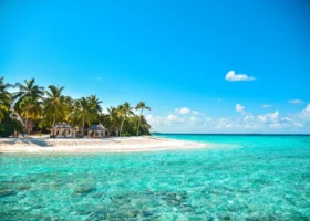 Lingua di sabbia bianca con palme da cocco inclinate, gazebo e lettini in legno, lambita da una laguna cristallina color acquamarina dal fondale trasparente sotto il cielo azzurro, sull'isola di Filaidhoo del Reethi Faru Resort, Atollo di Raa, Maldive, Oceano Indiano.