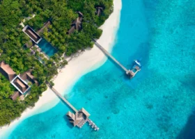 Veduta aerea del lungo pontile in legno che attraversa la laguna turchese dell'Isola di Vakkaru, collegando i padiglioni dal tetto in strame e la piscina a un attracco su palafitte con idrovolante ormeggiato; sabbia bianca e fitto palmeto di cocco, Atollo di Baa, Riserva della Biosfera UNESCO.